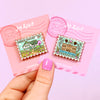 Hand Holding Enamel Pins of Pemberley Jane Austen Proie and Prejudice, and Anne of Green Gables