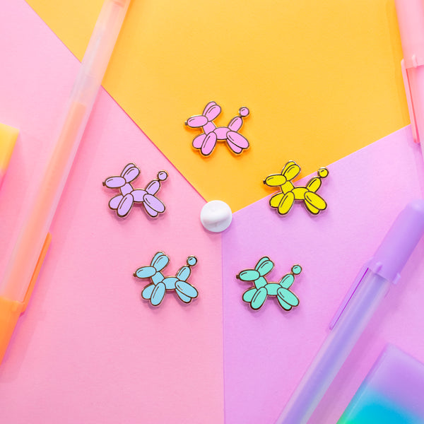 Balloon Dog Enamel Pins in Yellow, Teal, Blue, Pink and Purple on colorful paper.