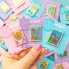 Hand holding set of stamp enamel pins displaying The Castle, The Tower and Atlantica. Mix and Match Pins displayed in background are, Porthaven, Neverland, A Galaxy Far Far Away, Tulgey Woods, The Magical Castle, Wizard of Oz, The Safari Dinosaur Island, The Wardrobe, Bag End