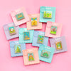 Colorful Display of Mix and Match Stamp Enamel Pin Set, Porthaven, Neverland, A Galaxy Far Far Away, Tulgey Woods, The Magical Castle for Wizards, Pemberley, Wizard of Oz, The Safari Dinosaur Island, The Wardrobe, Bag End, Dune, Anne of Green Gables
