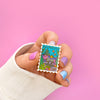 Hand Holding the Atlantica Stamp Enamel Pin.